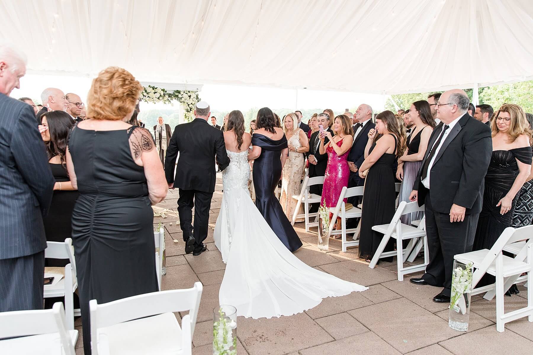 A bride and groom gracefully walk down the aisle in a charming tent at one of the most enchanting NJ wedding venues.