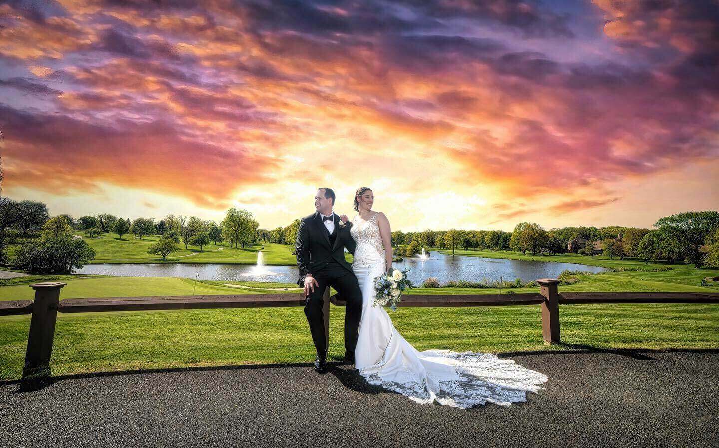 sunset-bride-groom-fence A beautiful bride and groom posing in front of a serene lake at sunset in one of the stunning New Jersey wedding venues.