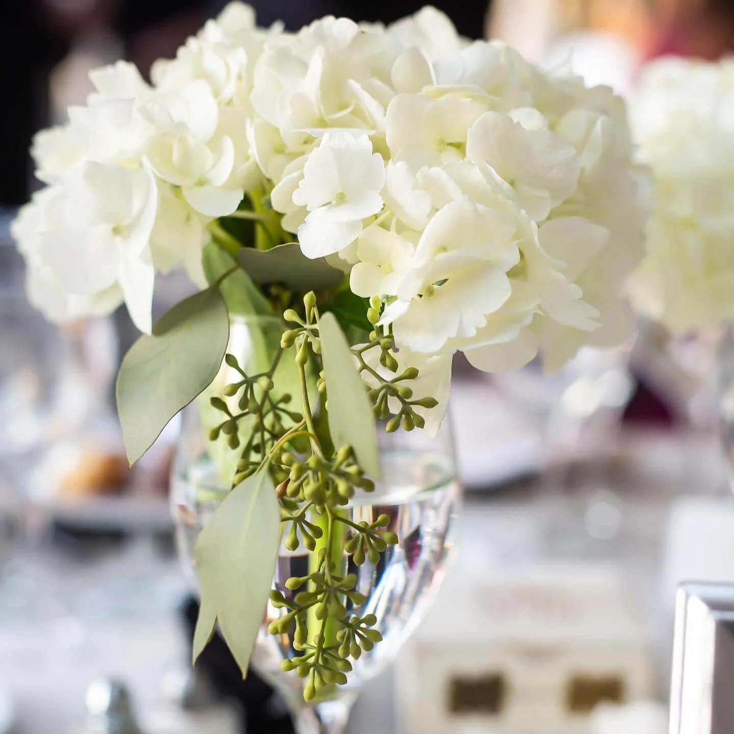 A vase of white hydrangeas and greenery on an elegantly set table at a kosher wedding in NJ.