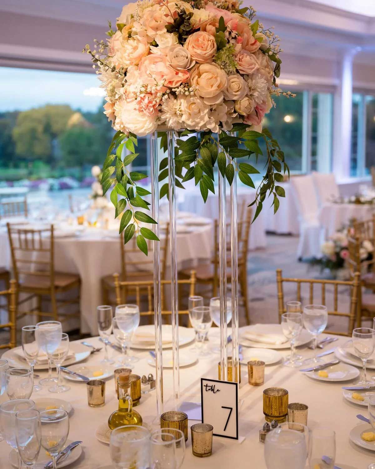 Elegant banquet table set with glassware, gold accents, and a tall floral centerpiece of pink and white flowers with greenery; table number 7 is displayed in the center at this stunning NJ wedding & event venue.