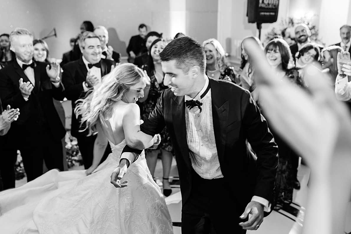 A bride and groom dance together in the center of a crowd of guests who are clapping and smiling at their NJ Kosher Wedding reception.